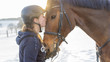 Frau Reiterin küsst Hannoveraner Pferd vor Schneelandschaft