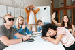 © Anton - Tired teacher standing near board and holding his hands on head. Group of young students making photos,listening music and sleeping during lesson. Students ignoring young teacher on lesson