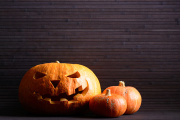 Halloween pumpkin with scary face and two little pumpkins on the background of wooden slats