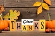 Give Thanks wood sign with pumpkins and leaves against a rustic wooden background
