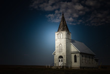 Horizontal Image Of A Bright Light Shining On An Old White Country Church In The Late Evening And Night Time.