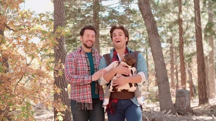 Wall Mural - Male parents in forest with baby in sling pass out of shot