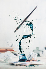 spilled ink flying above inkwell in a spiraling splash with tiny drops and flying pen on a light bac