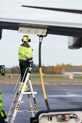 Wall Mural - Male Worker Refueling Airplane While Standing On Ladder