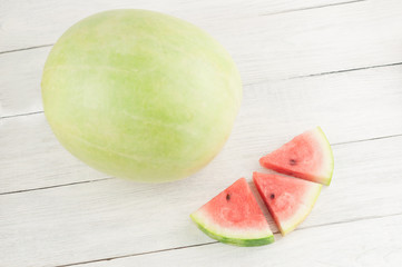 Three slices beside whole fresh ripe watermelon on old wooden rustic white table