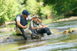 Father and son fly-fishing in river, sitting on rocks
