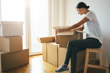 Wall Mural - Young woman unpacking moving boxes into new home