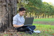 © tuaindeed - Young relaxed man is using a laptop at the outdoor park. Relax and technology concept.