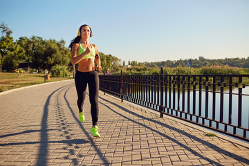 A sports girl in headphones runs through the park. Healthy lifestyle.