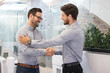© Bojan - Two smiling businessmen shaking hands together while standing in modern office.