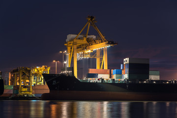 container cargo freight ship with working crane bridge in shipyard at twilight