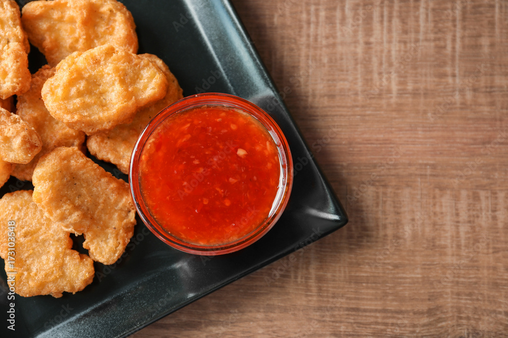 Plate with chicken nuggets and chili sauce on kitchen table