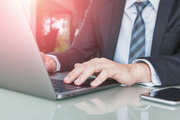 Hand of Businessman typing on laptop with smartphone and coffee cup in home office or co working space.Concept of workplace using mobile technology.