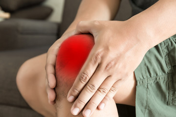 the knee man holds on suffering from pain in knee Closeup. The lesion is highlighted in red.