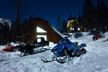 Wall Mural - Snowmobile from house chalets in winter forest with snow in light moon and starry sky