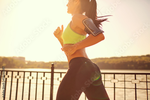Plakat Dziewczyna sportowa biegnie przez park nad jeziorem. Widok zza joggingu kobiety.