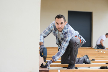 handsome young man carpenter installing a wood floor outdoor terrace in new house construction site