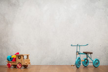 Retro Old Toy Tricycle And Obsolete Wooden Truck With Construction Blocks Front Concrete Textured Wall Background. Vintage Style Filtered Photo