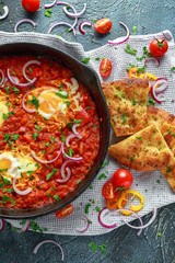 Wall Mural - Tasty Breakfast Shakshuka in a Iron Pan. Fried eggs with tomatoes, red, yellow peppers, onion, parsley, Pita bread and herbs. Healthy Food