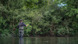 © annieze - Angler mit Wathose und Fliegenrute im Wasser beim Angeln bei Sonne im klaren Fluss stehend und werfend