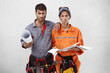 © WHstudio Leushin N - Picture of angry young man and woman professional builders in overalls holding papers and looking at camera with furious and mad expressions on their faces, unhappy with amount of work they have to do