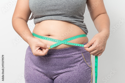 Zdjęcie XXL Z nadwagą kobieta sprawdza out jego ciało sadło z zieloną pomiarową taśmą dla otyłości na szarym tle, Zdrowy pojęcie