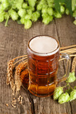 Fototapeta Zwierzęta - glass of foamy beer with hop cones and wheat on old wooden background