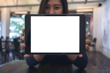 Canvas Print - Mockup image of a business woman holding and showing black tablet with blank white screen in cafe