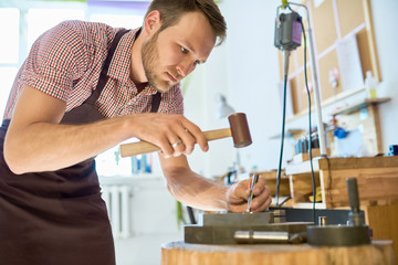 Wall Mural - Portrait of young man working with metal in  workshop, forming it with mallet hammer on work station with different tools