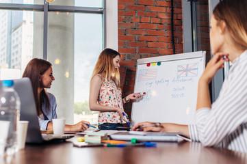 Teacher explaining differences between American and British spelling writing on whiteboard while adult students sitting at desk listening to her in stylish English language school