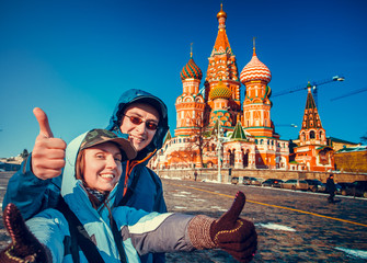 Happy tourists sightseeing city with fingers up next to Saint Basil's Cathedral. Red Square, Moscow, Russia. Holiday, travel, recreation. Winter season, bright colors, clear blue sky