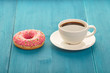 Pink donut with a cup of coffee on a wooden table. Sweet donut