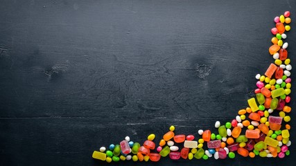  Colored candies, sweets and lollipops. On a black wooden background. Top view. Free space.