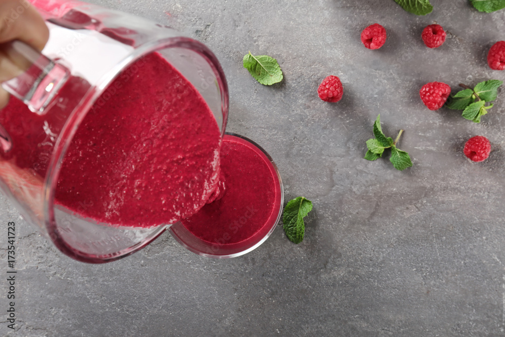 Pouring tasty smoothie into glass on table