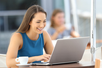 Wall Mural - Happy woman using a laptop in a bar terrace