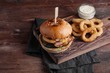 © Vasiliy - Closeup of a tasty Burger with appetizers such as fried onion rings with a white garlic sauce. Juicy Burger with bacon and cheese on a dark wood background