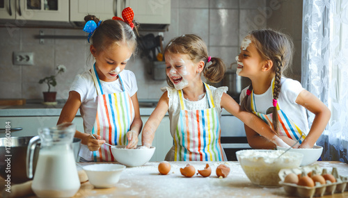 Cuadros en Lienzo happy sisters children girls bake cookies, knead dough, play with flour and laug
