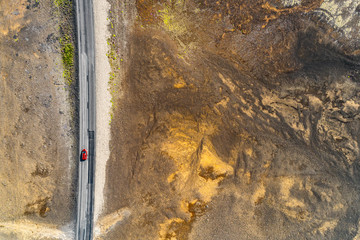 Open road with car driving on travel adventure aerial view of desert landscape for vacation concept. Highway crossing through lava rocks volcanic mountains, nature background in Iceland.