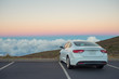 White car in mountains above the clouds at sunset or sunrise