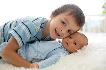 Wall Mural - Beautiful boy, hugging with tenderness and care his newborn baby brother at home