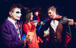 © VadimGuzhva - Halloween party. Two guys and a girl talk at a party with glasses with alcohol cocktails in their hands