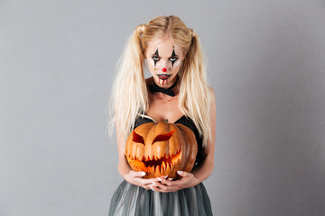 Frightening blonde woman in halloween make up holding carved pumpkin