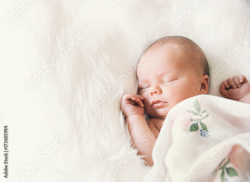 Fotografía Sleeping newborn baby in a wrap on white blanket.