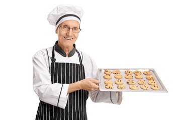 Wall Mural - Elderly baker holding a tray with freshly baked cookies