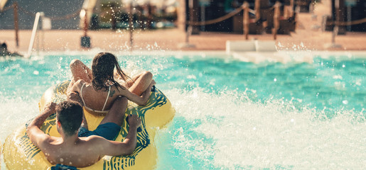 Cool people having fun on the water slide with friends and familiy in the aqua fun park glides playing happy and water splashes are all over. Blue sky background looks amazing sunlight