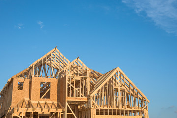 Close-up of gables roof on stick built home under construction and blue sky in Humble, Texas, USA. New build roof with wooden truss, post and beam framework. Timber frame house, real estate background