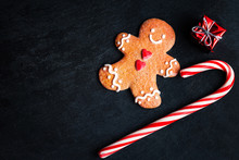 Christmas Decorations With Christmas Gift Box, Gingerbread Man Cookie And Candy Stripe Red Stick On Dark Background With Copyspace. Xmas Holiday Symbols