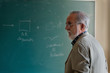 © Miquel Llonch/Stocksy - Mature professor in the classroom with green blackboard