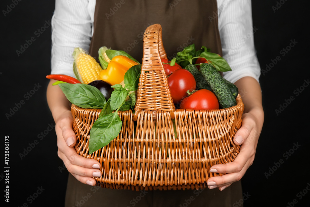 Woman holding wicker basket with fresh vegetables on black background