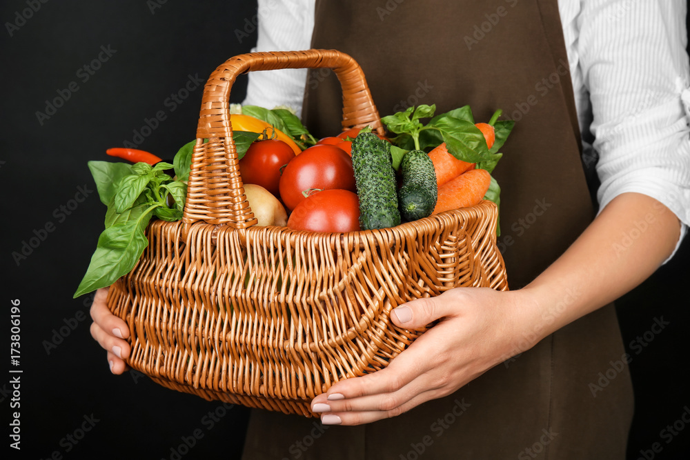 Woman holding wicker basket with fresh vegetables on black background